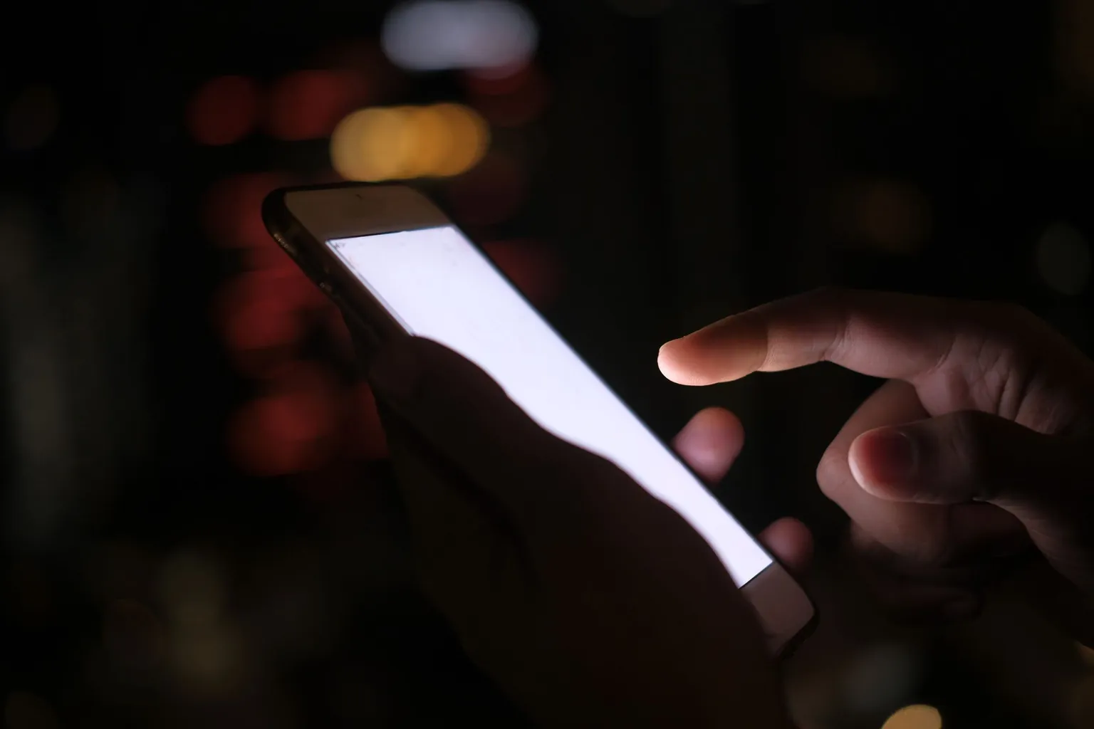 Main tenant un smartphone à l’écran allumé, dans la pénombre