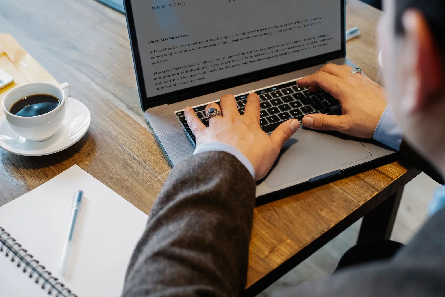 Mains tapant un courrier sur un ordinateur portable, à côté d’une tasse de café et d’un carnet