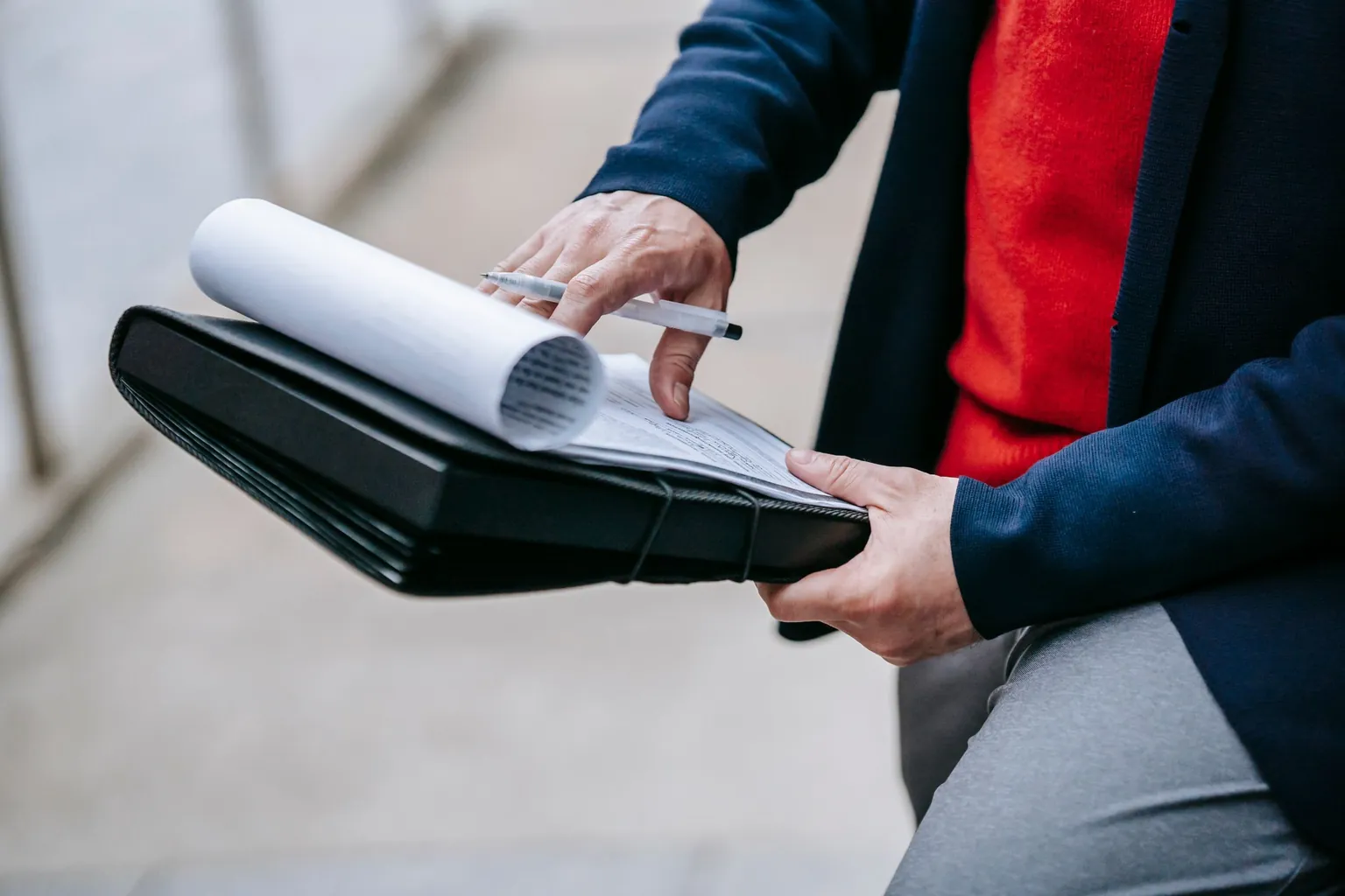 Mains tenant un porte-documents noir et feuilletant des papiers imprimés, un stylo entre les doigts