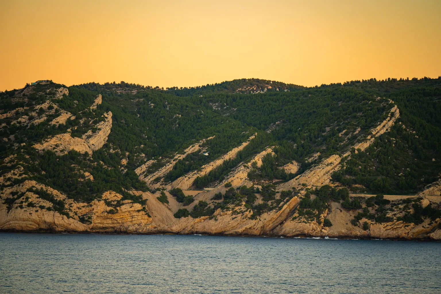Collines calcaires couvertes de pins plongeant dans la mer au coucher du soleil, sur la côte des calanques près de Marseille
