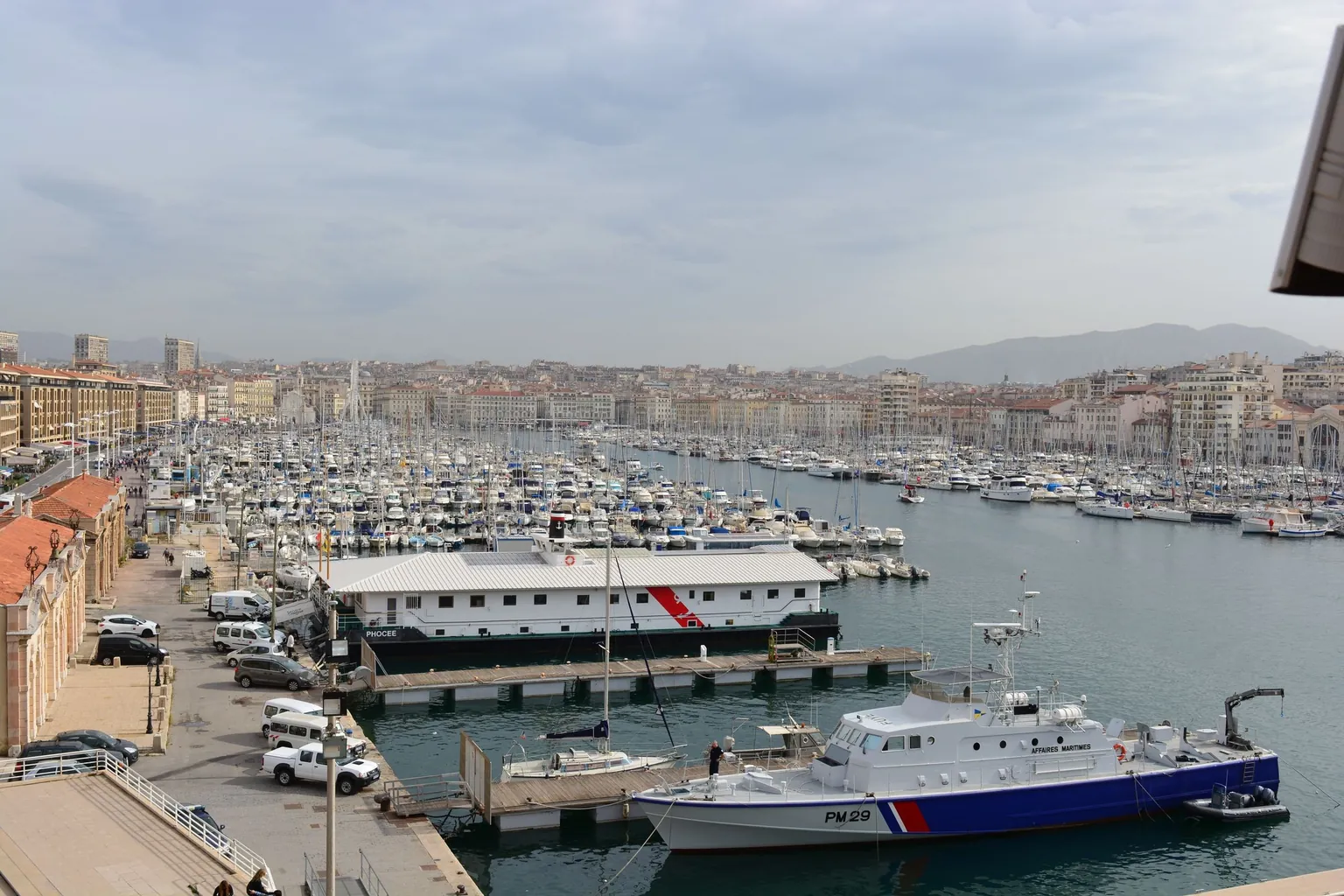 Vue en hauteur du Vieux-Port de Marseille, ses pontons chargés de voiliers, ses quais et les immeubles de la ville au pied des collines