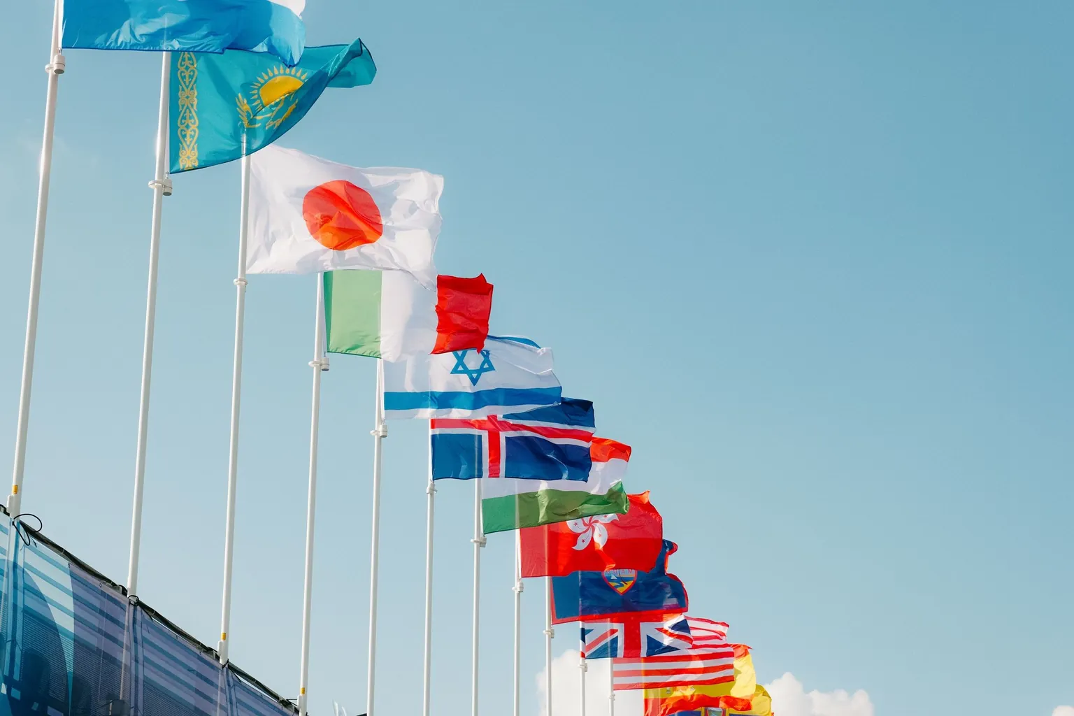 Rangée de drapeaux de différents pays et territoires, dont le Japon, l’Italie et Hong Kong, flottant sur des mâts