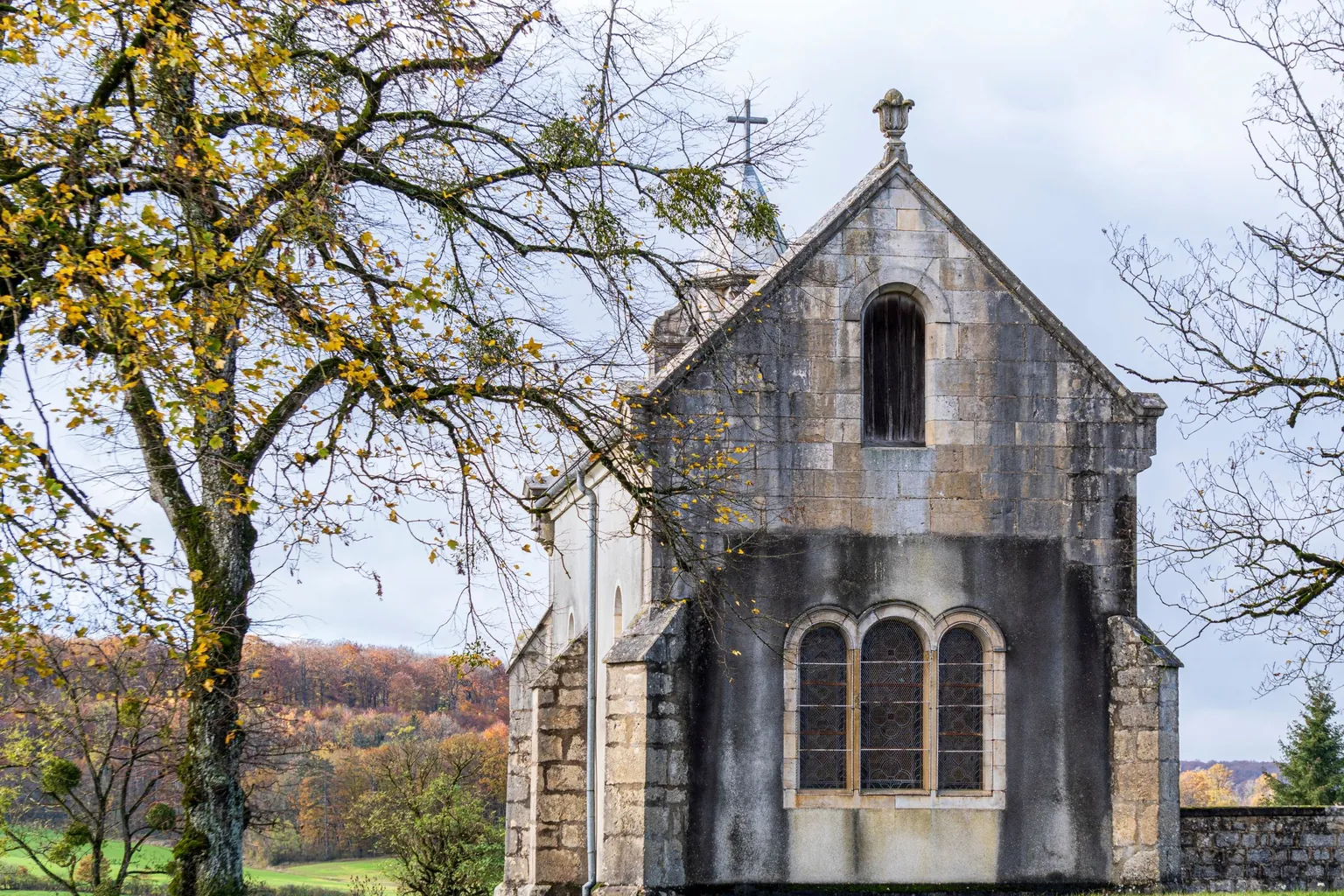 Chapelle de pierre surmontée d'une croix, entourée d'arbres aux feuilles d'automne