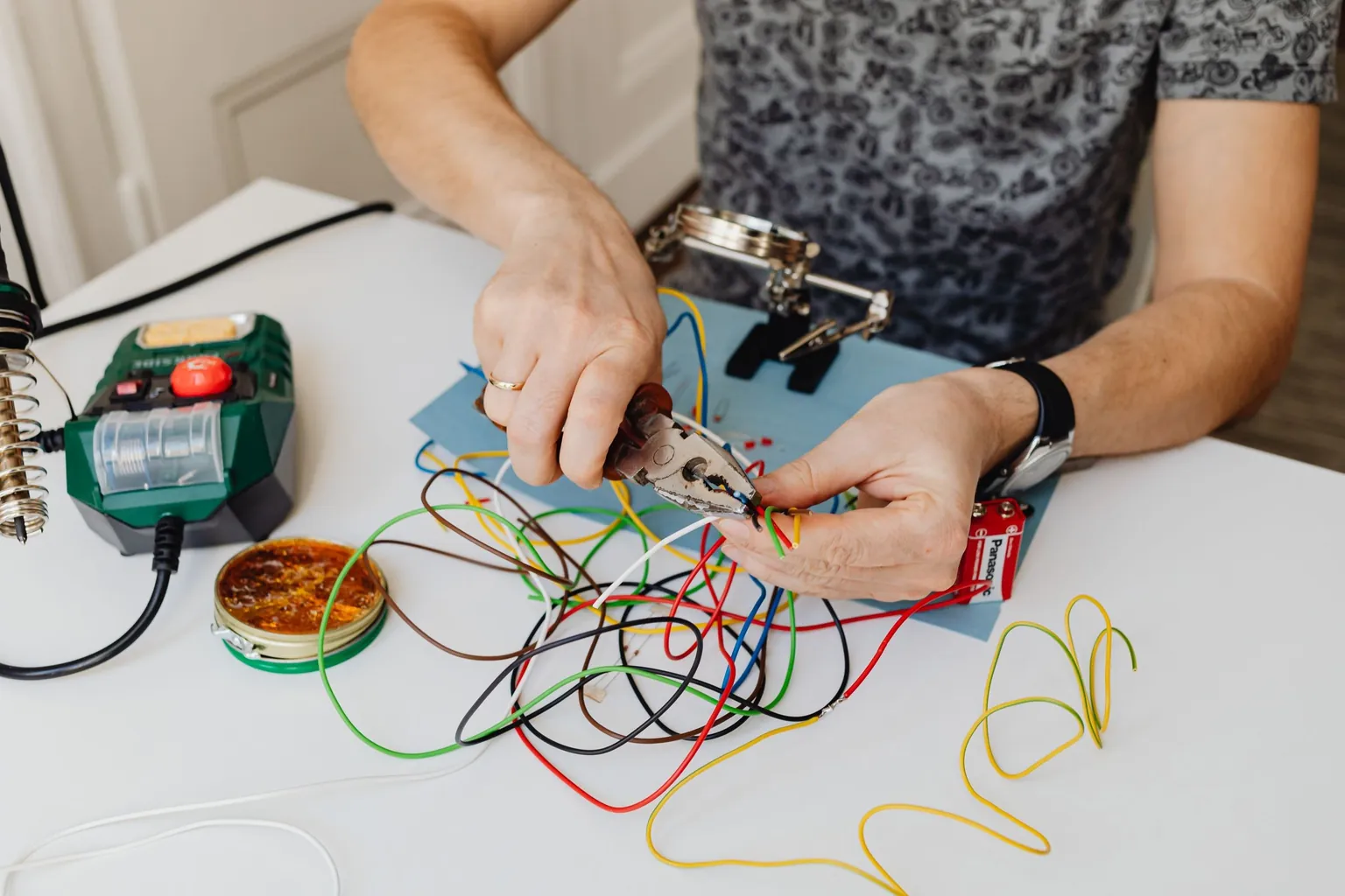 Mains dénudant des fils électriques de couleur à la pince, à côté d'un fer à souder