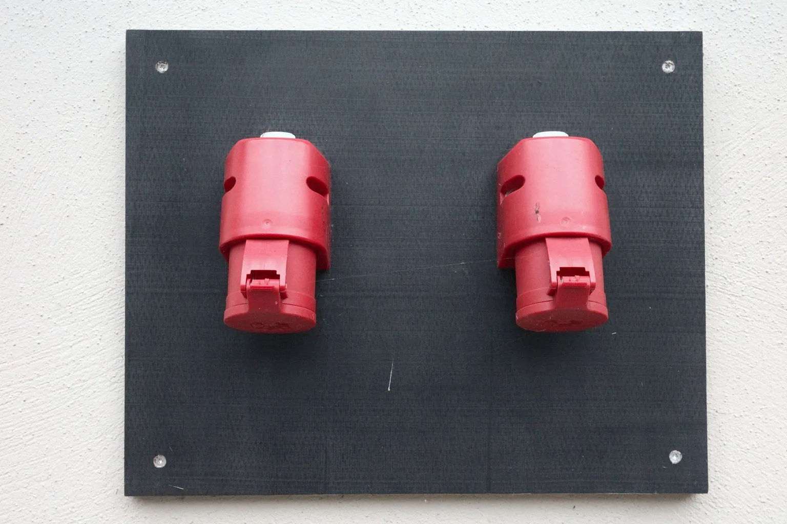 Deux prises électriques industrielles rouges fixées sur une plaque noire contre un mur extérieur