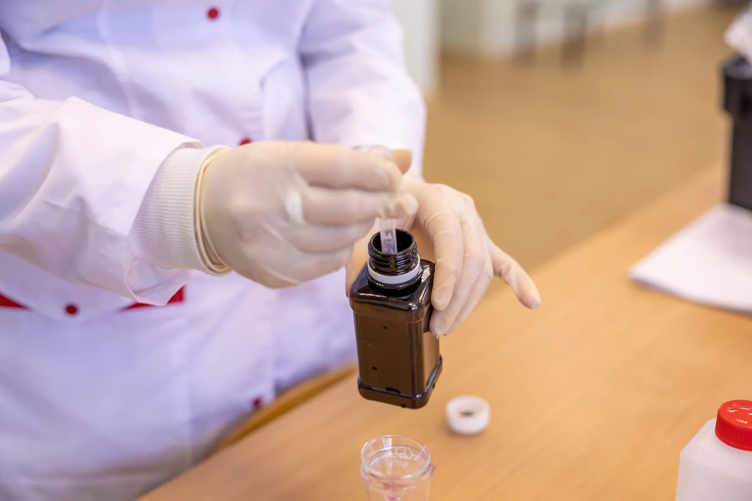 Mains gantées versant un liquide d'un flacon brun au-dessus d'un plan de travail