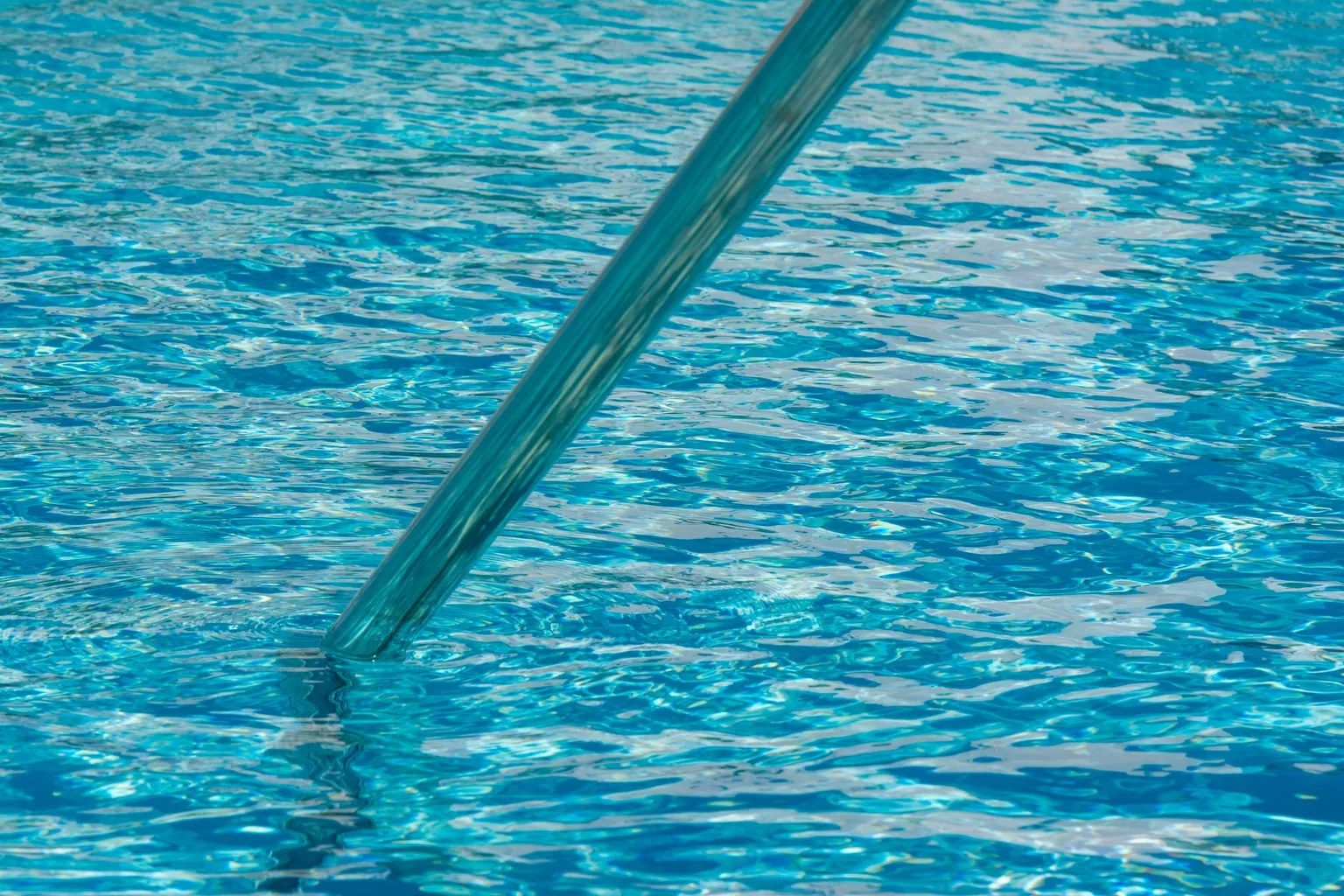 Main courante métallique plongeant dans l'eau bleue et limpide d'une piscine