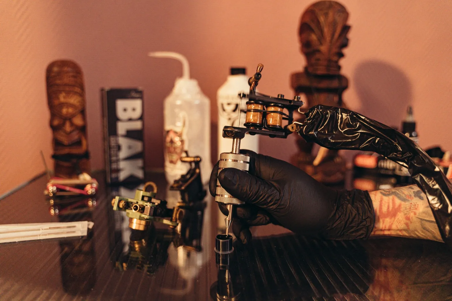 Main gantée de noir tenant une machine à tatouer à bobines au-dessus d'un godet d'encre, dans un studio