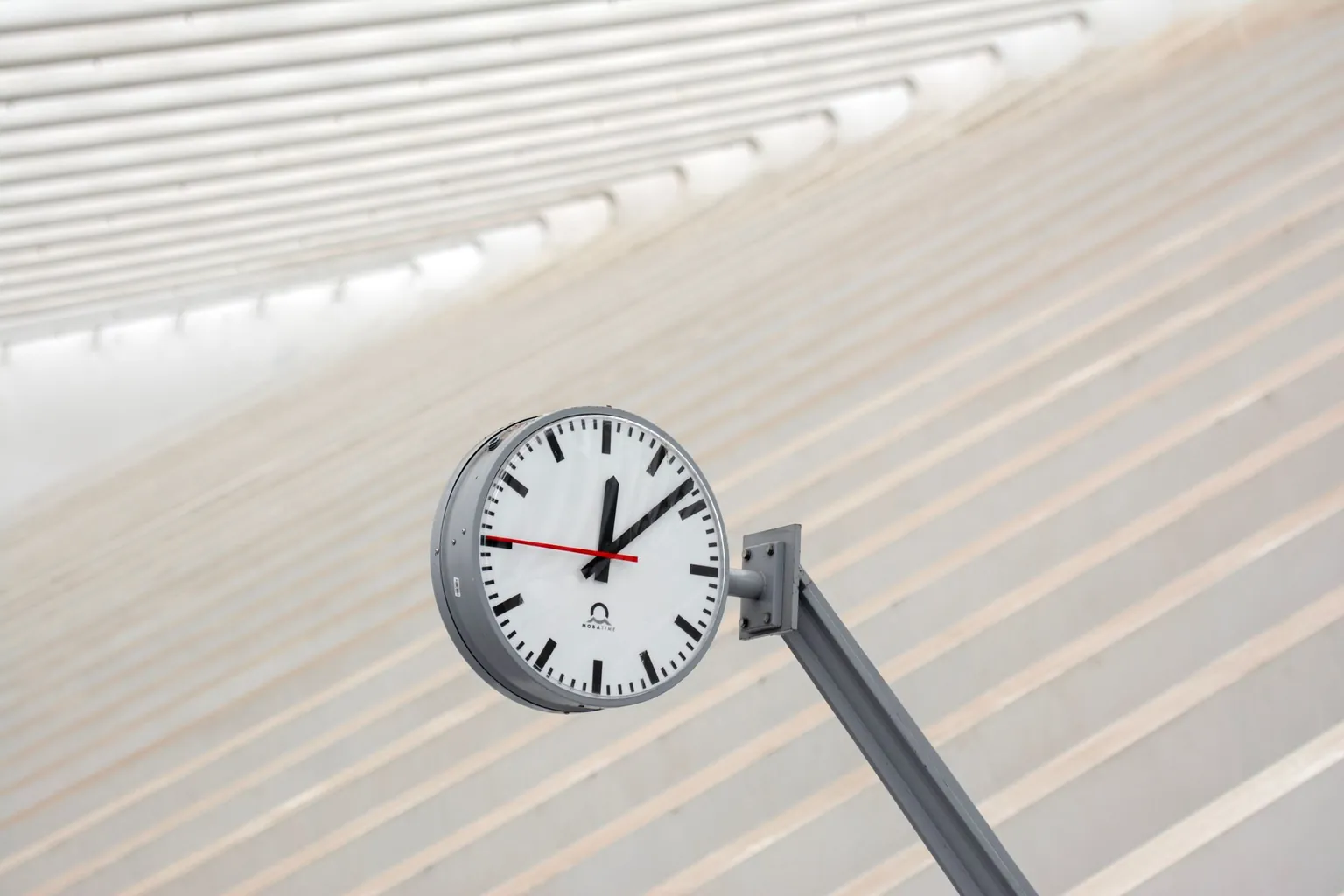 Horloge de gare ronde à aiguilles, trotteuse rouge, suspendue sous une verrière claire