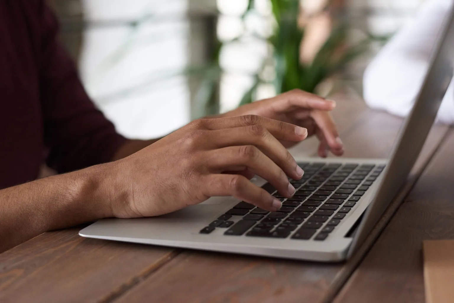 Mains tapant sur le clavier d'un ordinateur portable posé sur une table en bois