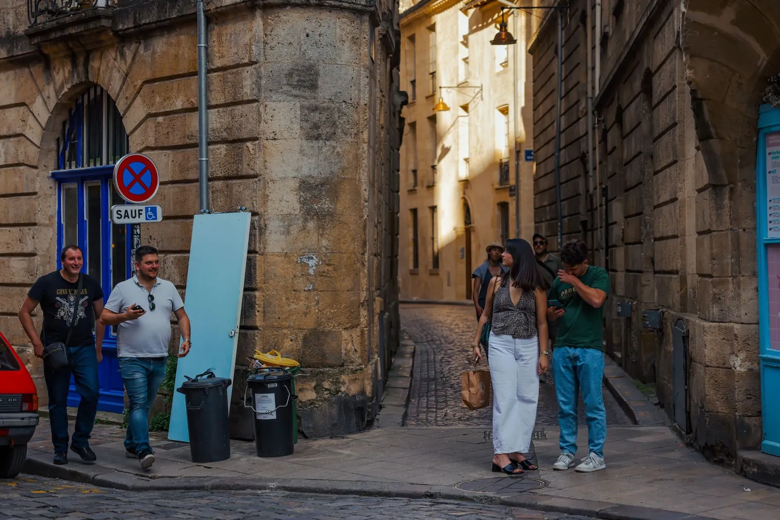 Rue pavée d'un quartier ancien aux façades de pierre blonde, avec un panneau d'interdiction de stationner sauf véhicules de personnes handicapées et une petite voiture rouge garée