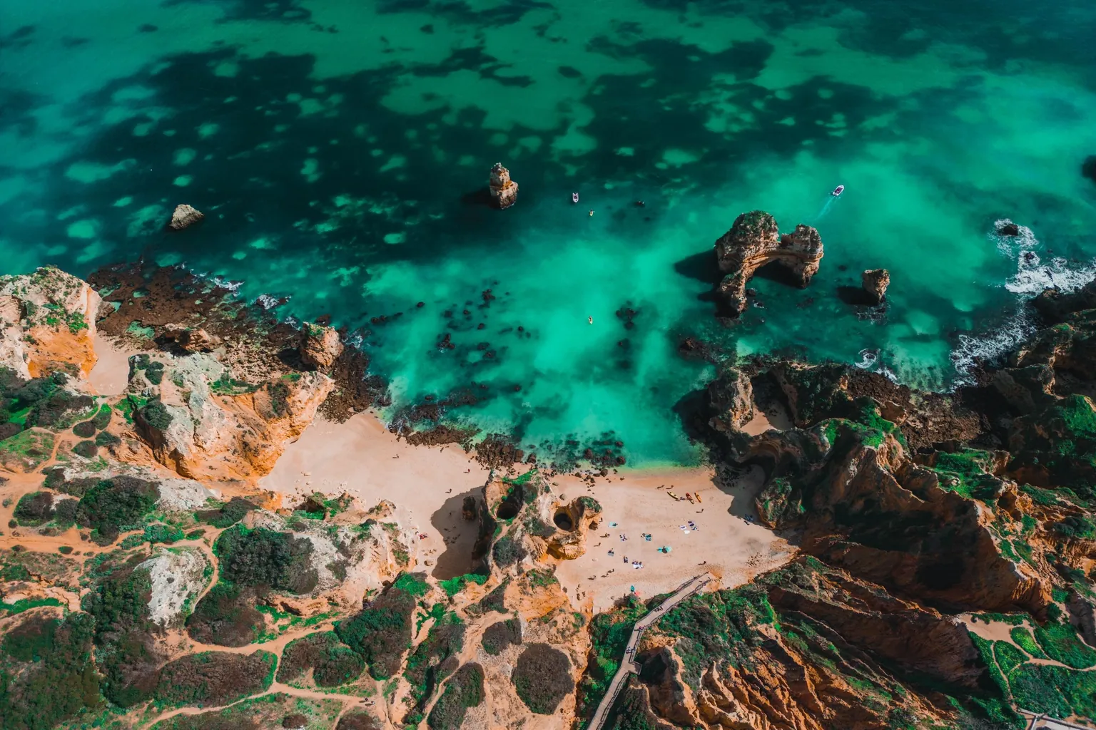 Vue aérienne d'une crique de sable entre des falaises ocre, face à une mer turquoise