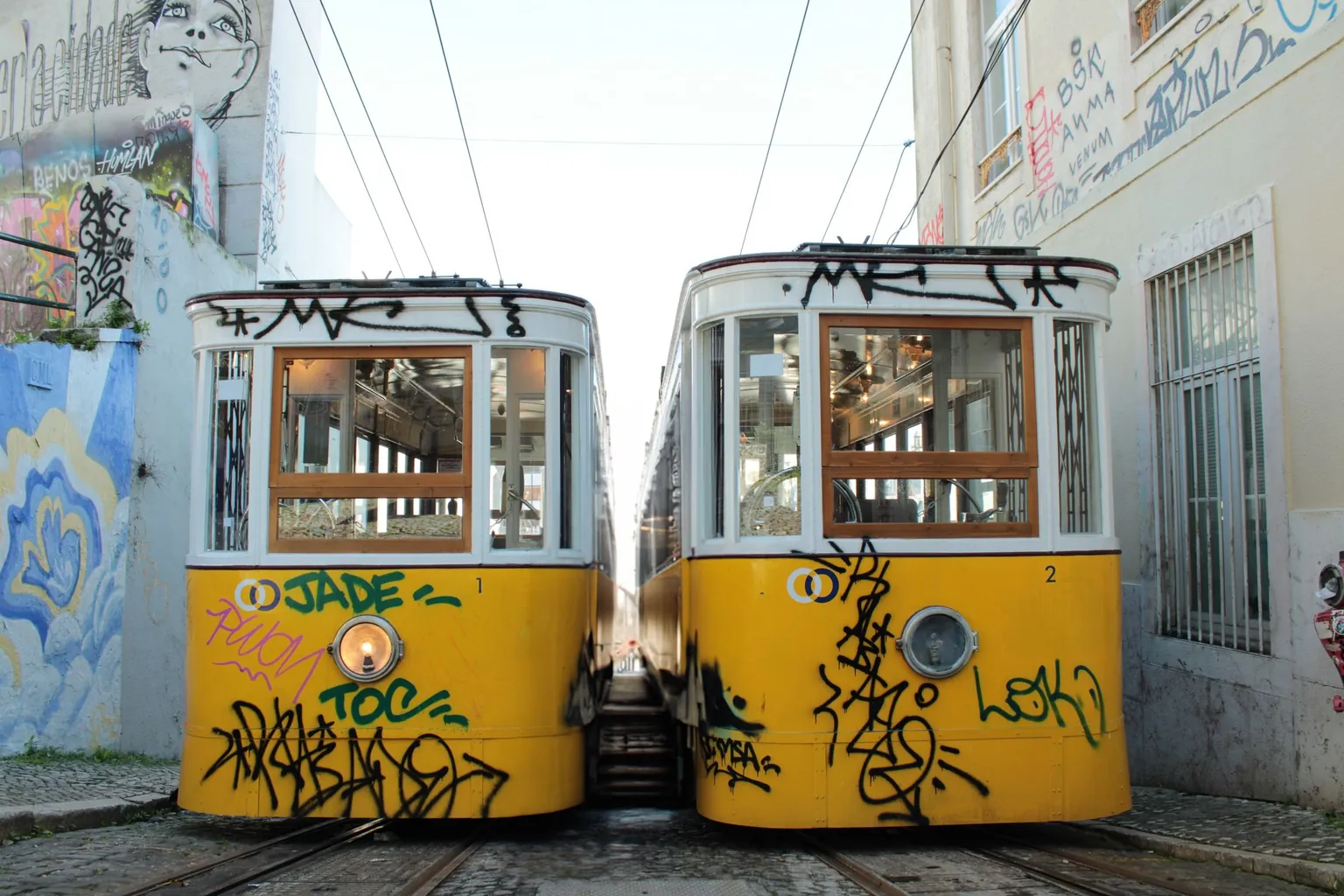 Deux voitures jaunes de funiculaire couvertes de graffitis, côte à côte dans une rue pavée en pente