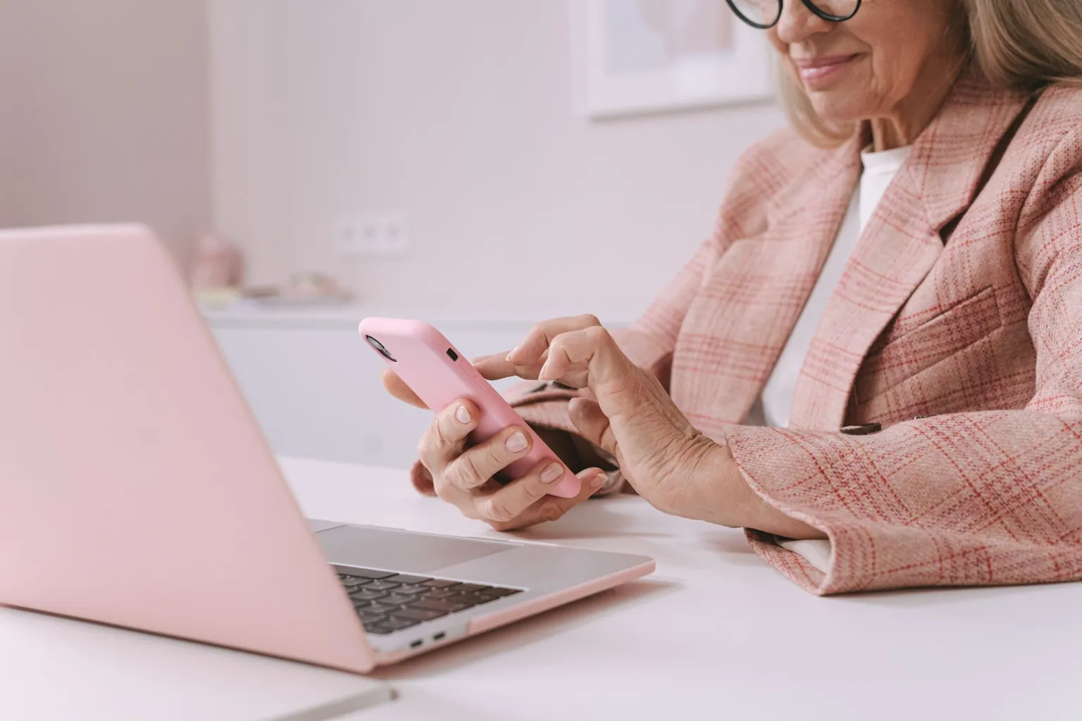 Femme en veste à carreaux roses tapant sur son smartphone devant un ordinateur portable