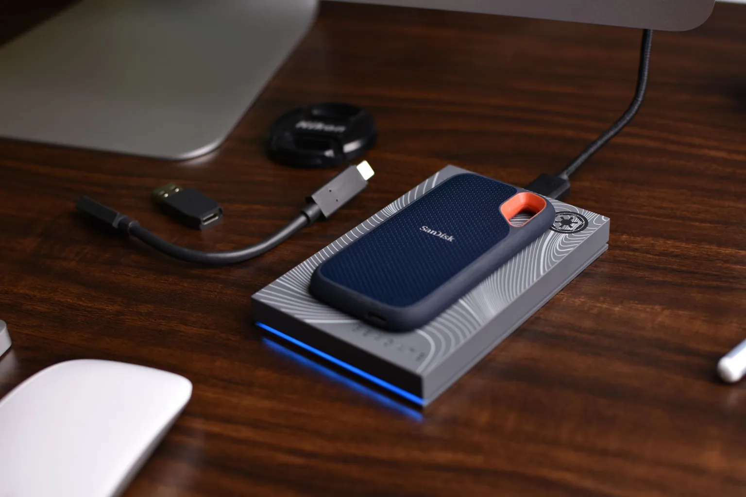 Disque dur externe et SSD portable posés sur un bureau, à côté de câbles USB