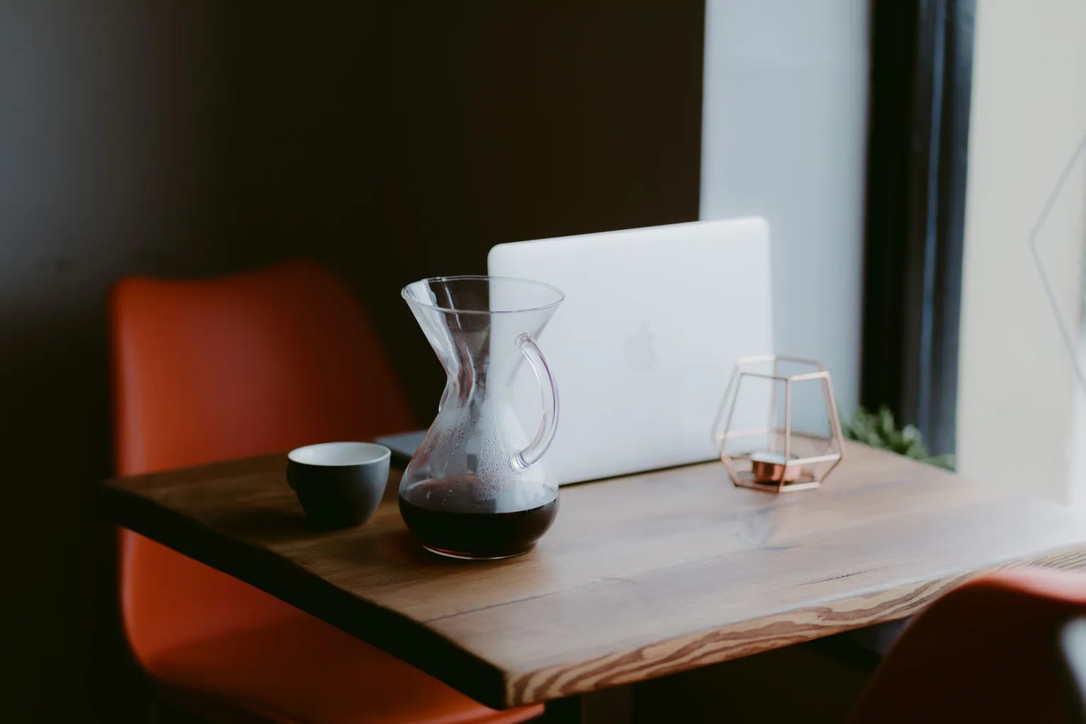 Ordinateur portable fermé sur une table en bois, à côté d'une carafe de café et d'une tasse