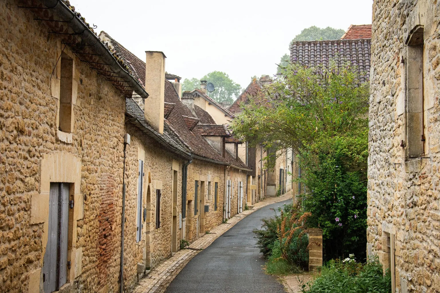 Ruelle étroite d'un village bordée de maisons anciennes en pierre blonde aux toits de tuiles