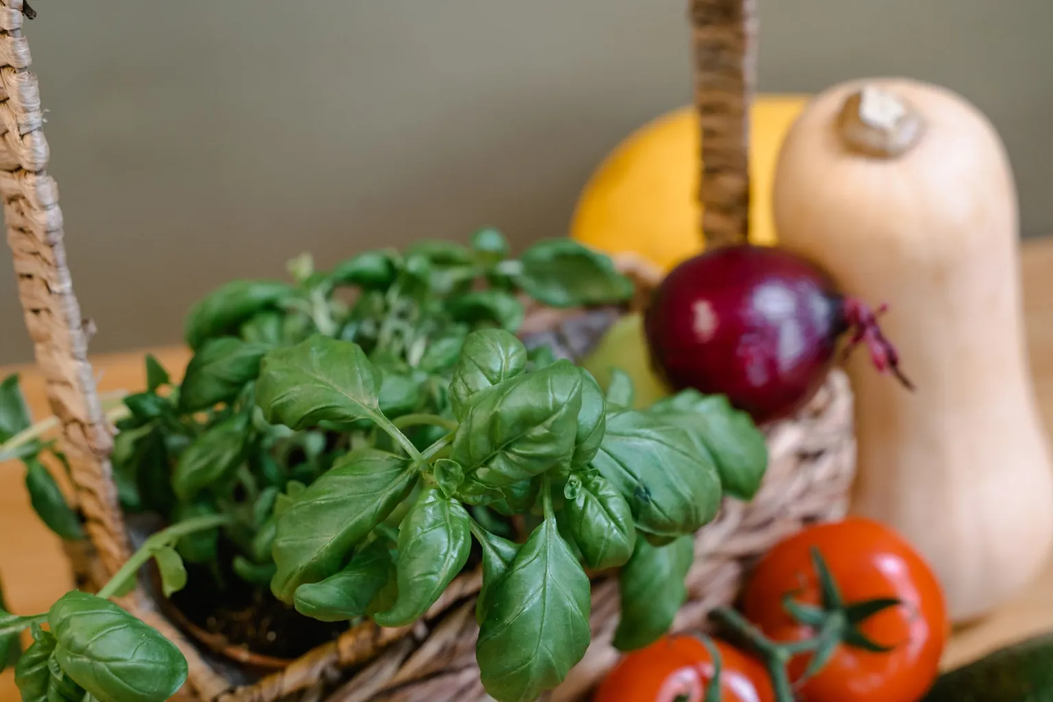 Panier tressé garni de basilic, d'oignon rouge, de tomates et de courges