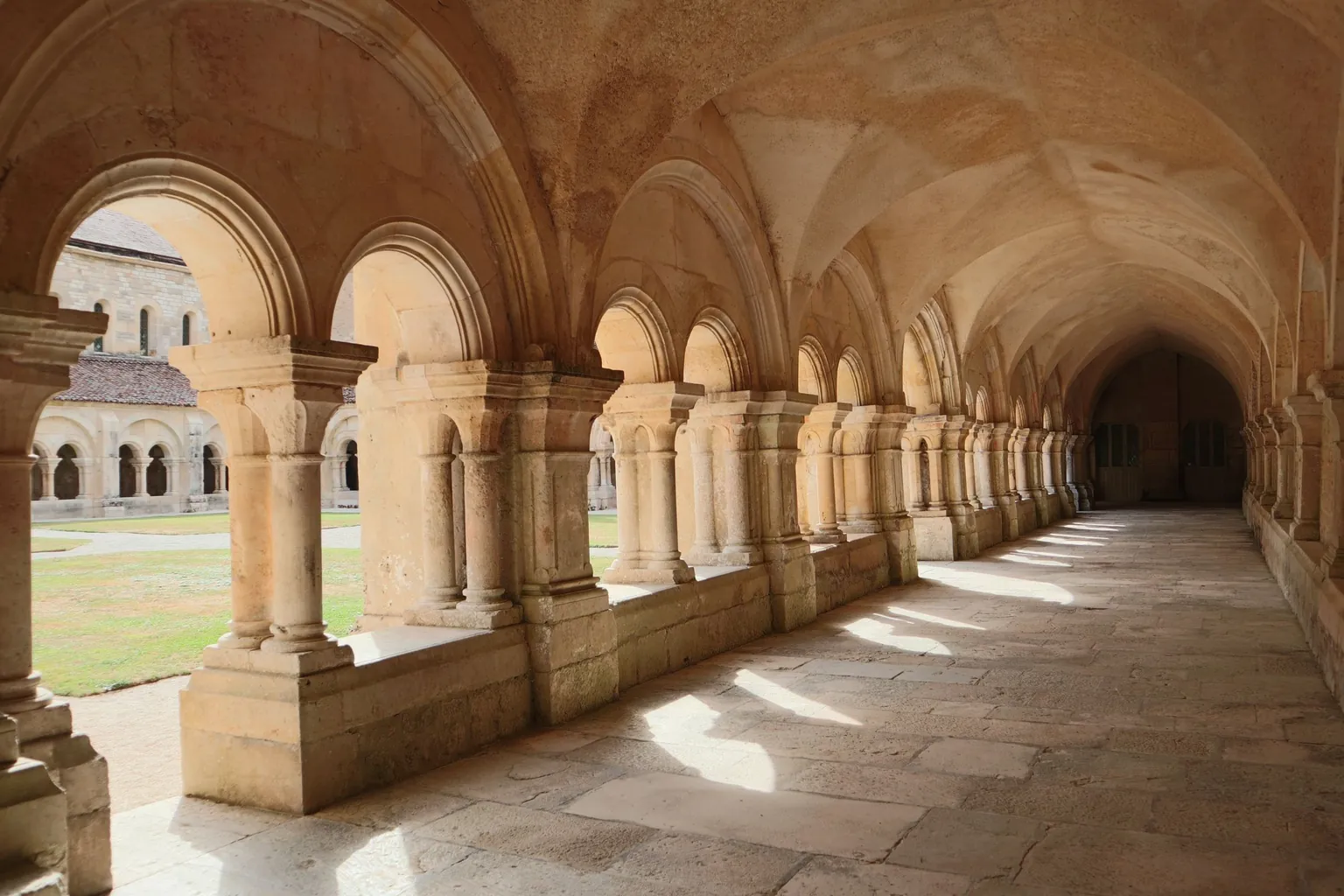 Galerie voûtée d'un cloître roman en pierre blonde ouverte sur un préau gazonné